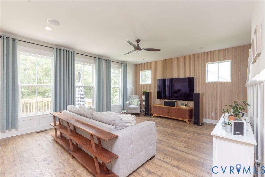 Wood-finish flooring, recessed ceiling lighting, three windows with white trim, ceiling fan, and a wood-slat accent wall