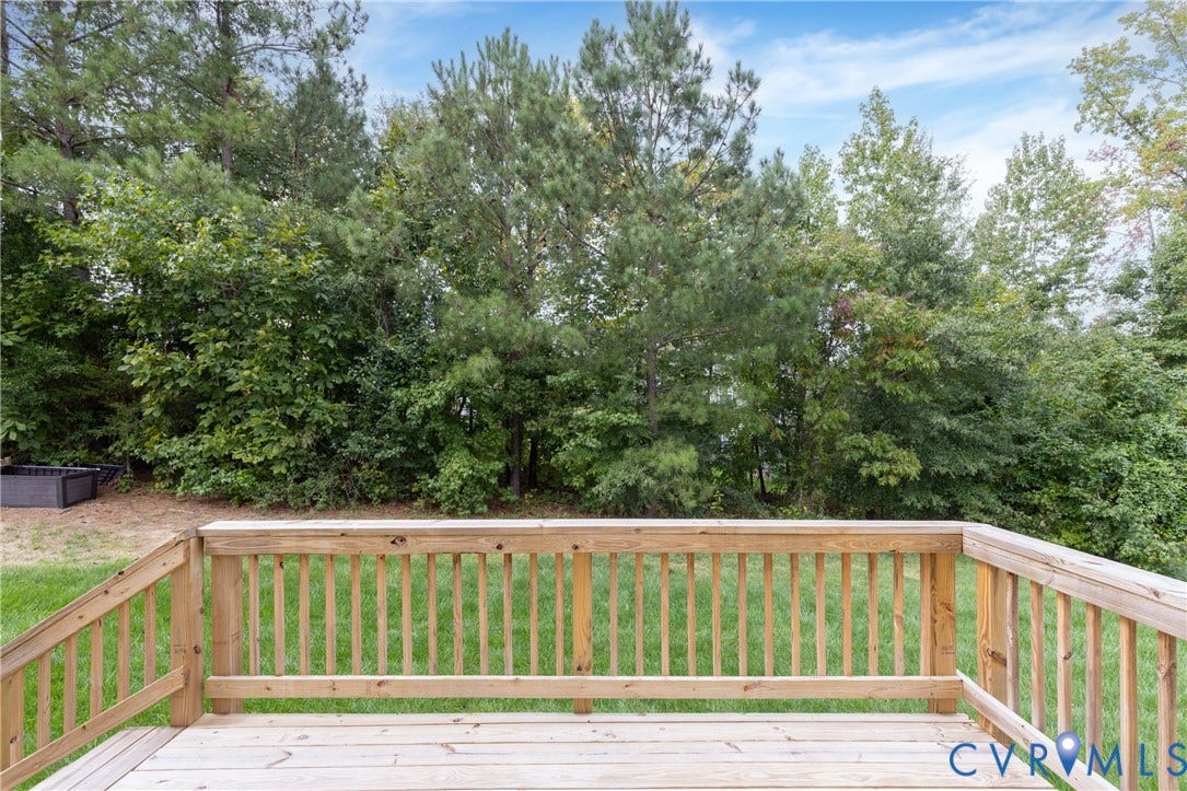 Wood deck with railings overlooking a grassy area and mature trees