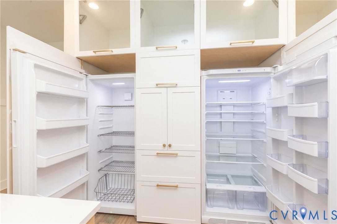 Integrated refrigerator and freezer units, custom white cabinetry with gold-finish hardware, built-in overhead lighting, and clear glass-front upper cabinets