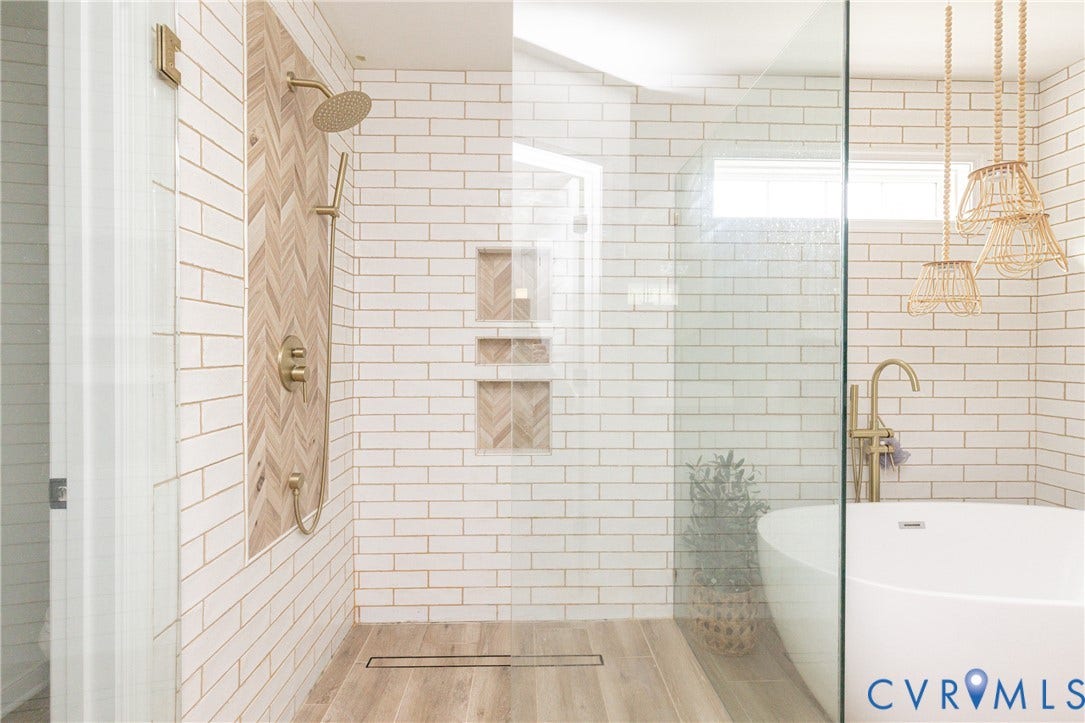 Walk-in shower with gold-tone fixtures, herringbone tile accent wall, built-in shower niches, and wood-finish flooring