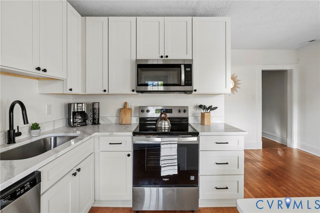 2931 W Leigh Street, Scotts Addition, Richmond, VA 23230 White shaker-style cabinetry with matte black hardware, stainless steel appliances, solid surface countertops, a stainless steel sink with a matte black gooseneck faucet, and wood-finish flooring