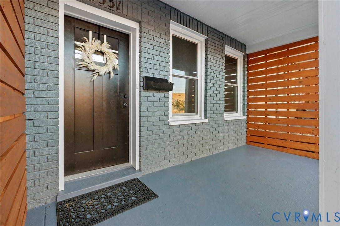 2931 W Leigh Street, Scotts Addition, Richmond, VA 23230 Front entry with a dark-paneled door, gray brick facade, and two windows with white trim