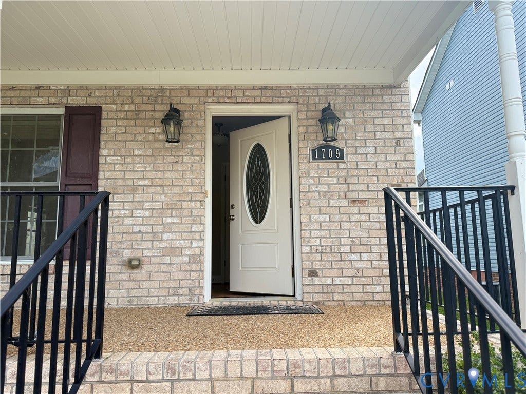 1709 Kemper Street, Richmond, VA 23220 Brick facade with a covered entry, featuring a white door with an oval glass insert, black exterior lighting, and black metal railings
