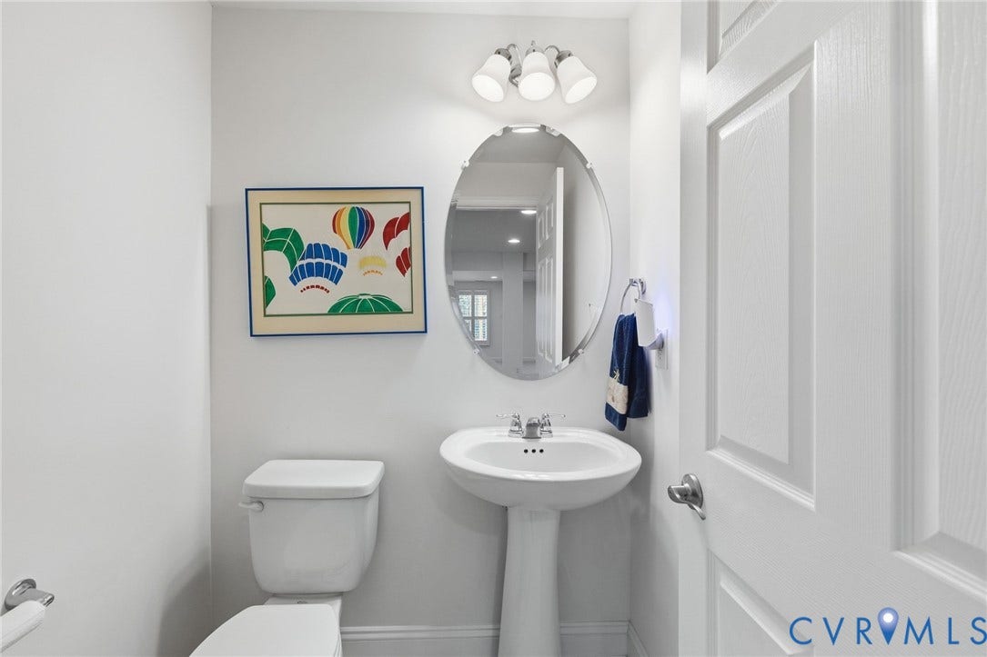 15750 Mosaic Creek Boulevard, Henrico, VA 23238 Pedestal sink with chrome fixtures and an oval mirror, illuminated by a three-light vanity fixture