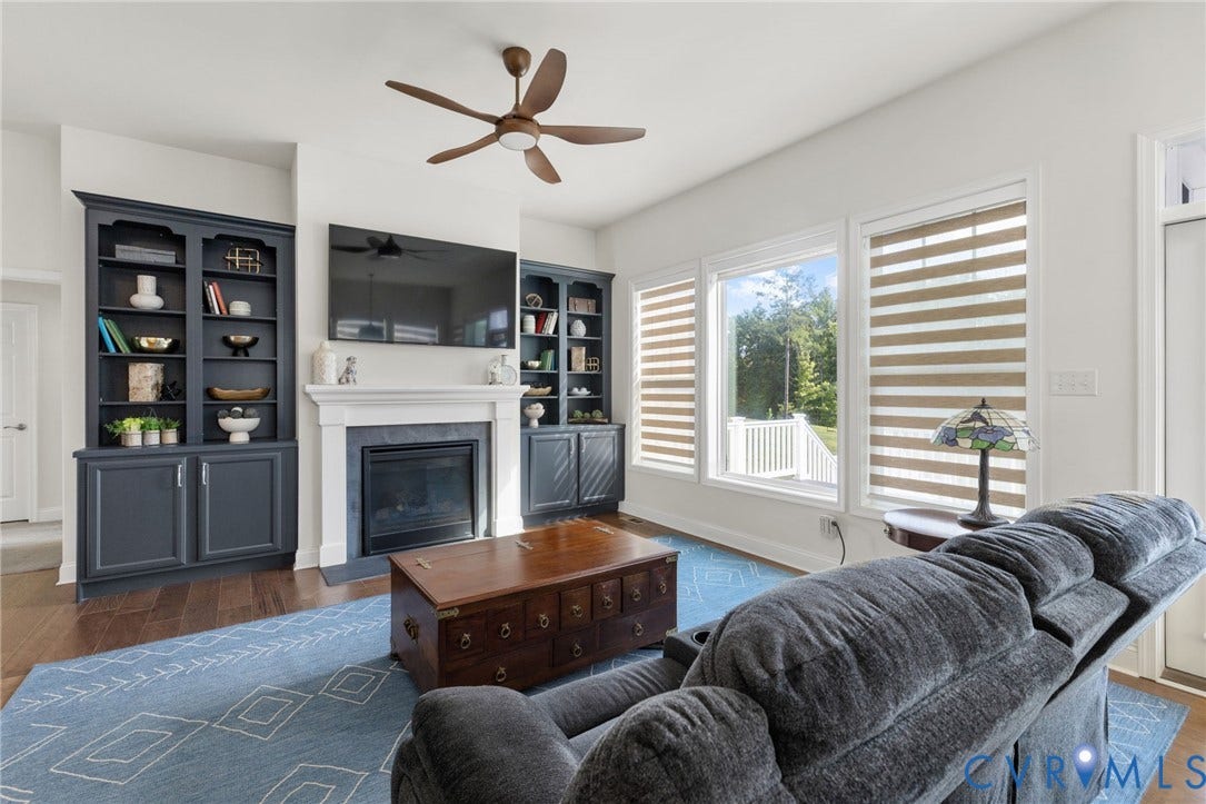 15750 Mosaic Creek Boulevard, Henrico, VA 23238 Living area featuring a ceiling fan, fireplace with a stone surround, built-in shelving, wood flooring, and multiple windows and custom remote controlled blinds