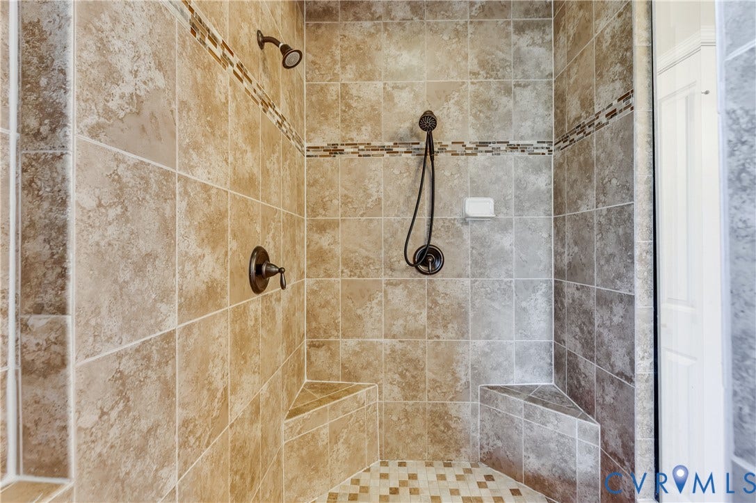 Tiled shower enclosure featuring a fixed shower head, handheld shower, and integrated bench seating