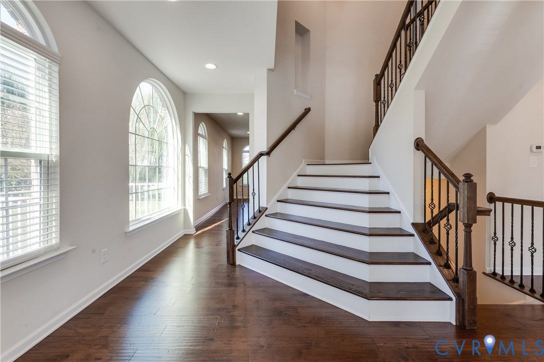Arch-top windows, wood-finish flooring, recessed lighting, and a staircase with wrought iron balusters and wood handrails