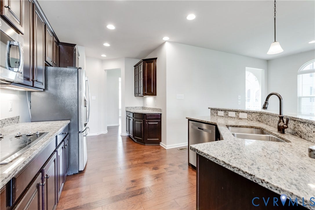 Kitchen featuring wood-finish flooring, dark wood cabinetry, light-toned countertops, and stainless steel appliances