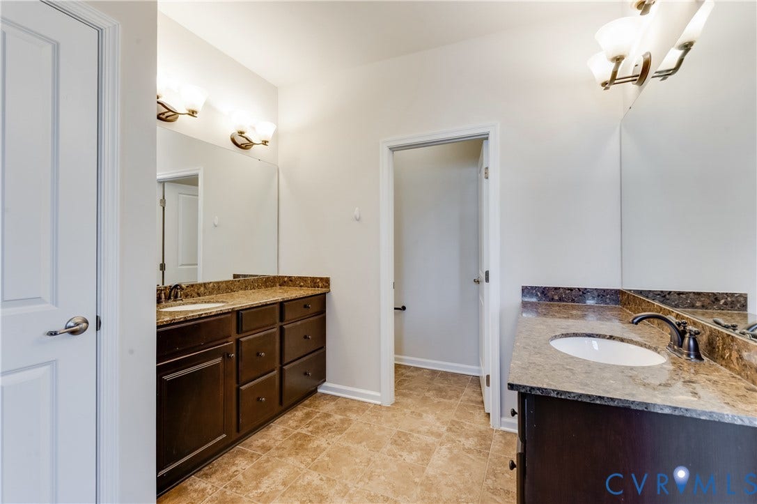 Dual vanities with stone countertops, undermount sinks, bronze-finish faucets, and integrated mirrors with sconce lighting