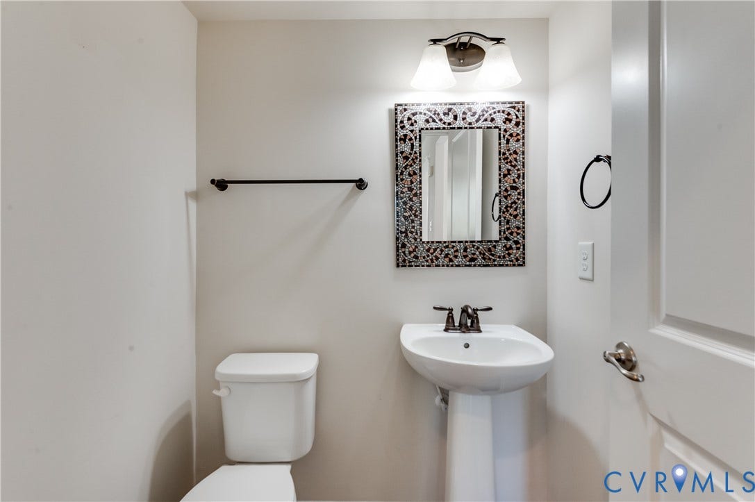 Compact powder room featuring a pedestal sink with chrome faucet, ceramic toilet, decorative framed mirror with ornamental detailing, ceiling-mounted light fixture, and black towel bar hardware