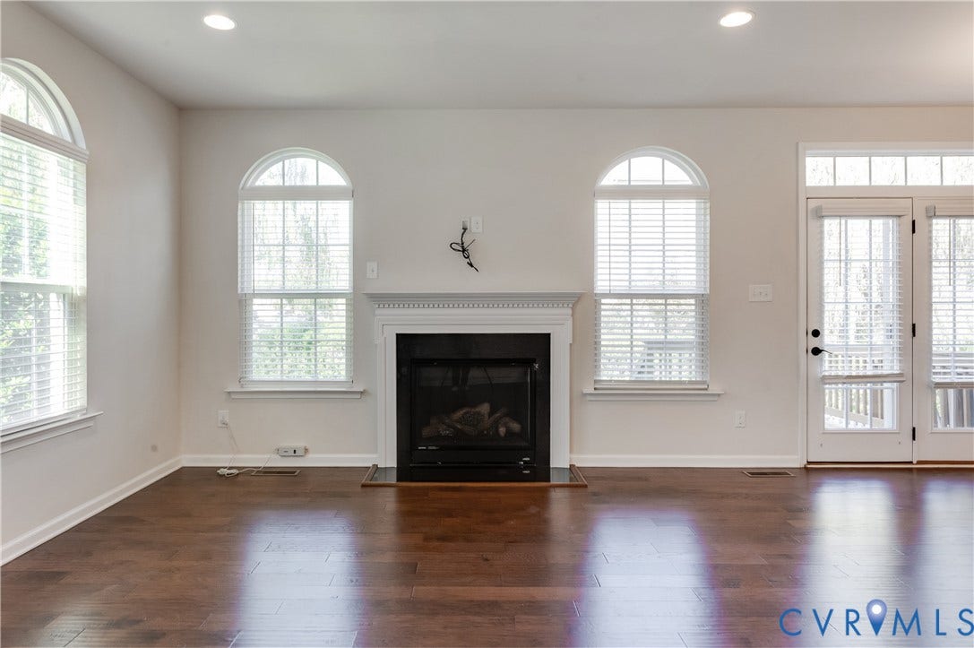 Gas fireplace with a classic mantel, wood-finish flooring, recessed lighting, and arched windows with blinds