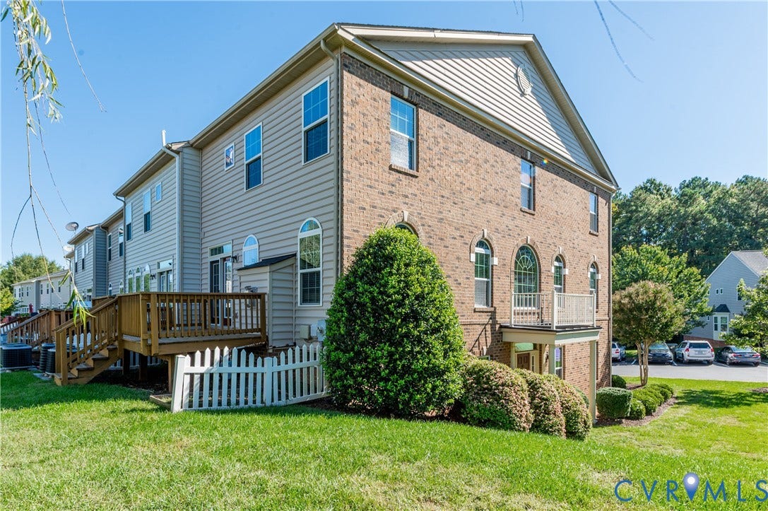 Brick and siding exterior featuring a multi-level wood deck, a white picket fence, and mature landscaping