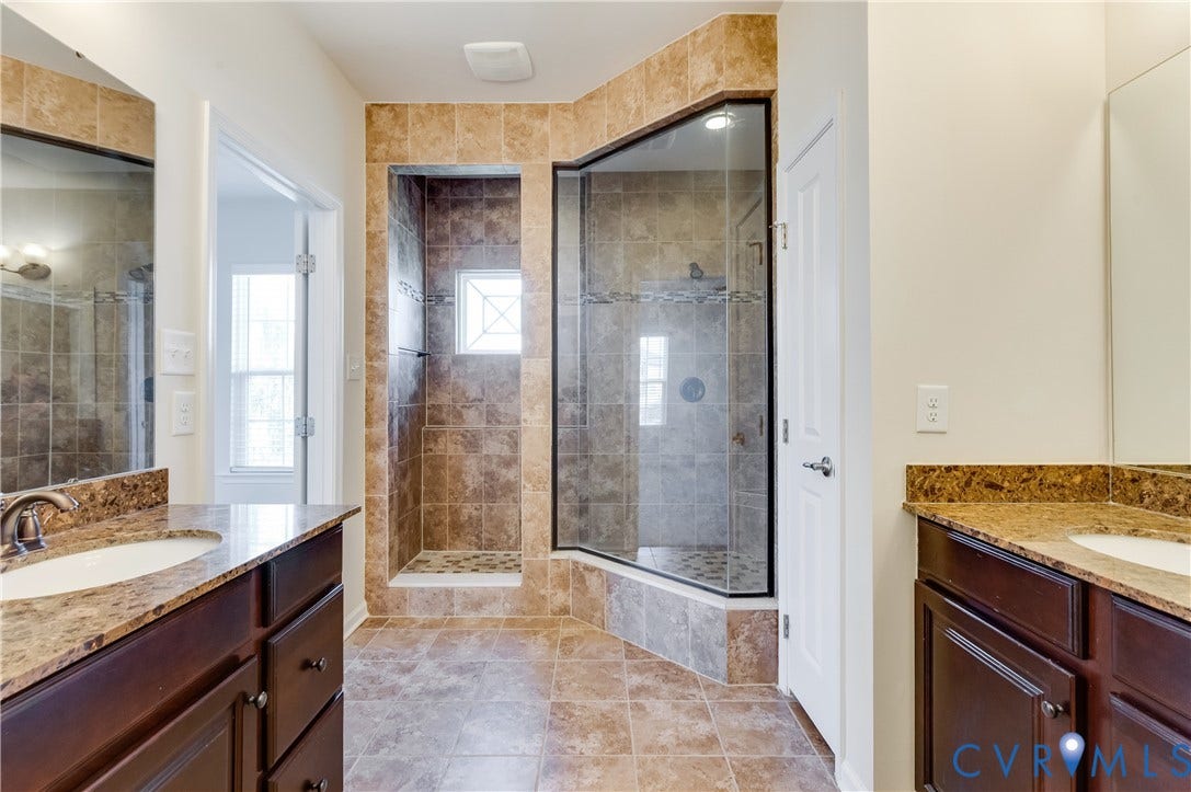 Spa-inspired primary bathroom featuring dual vanities with granite countertops, wood-finish cabinetry, and brushed nickel fixtures