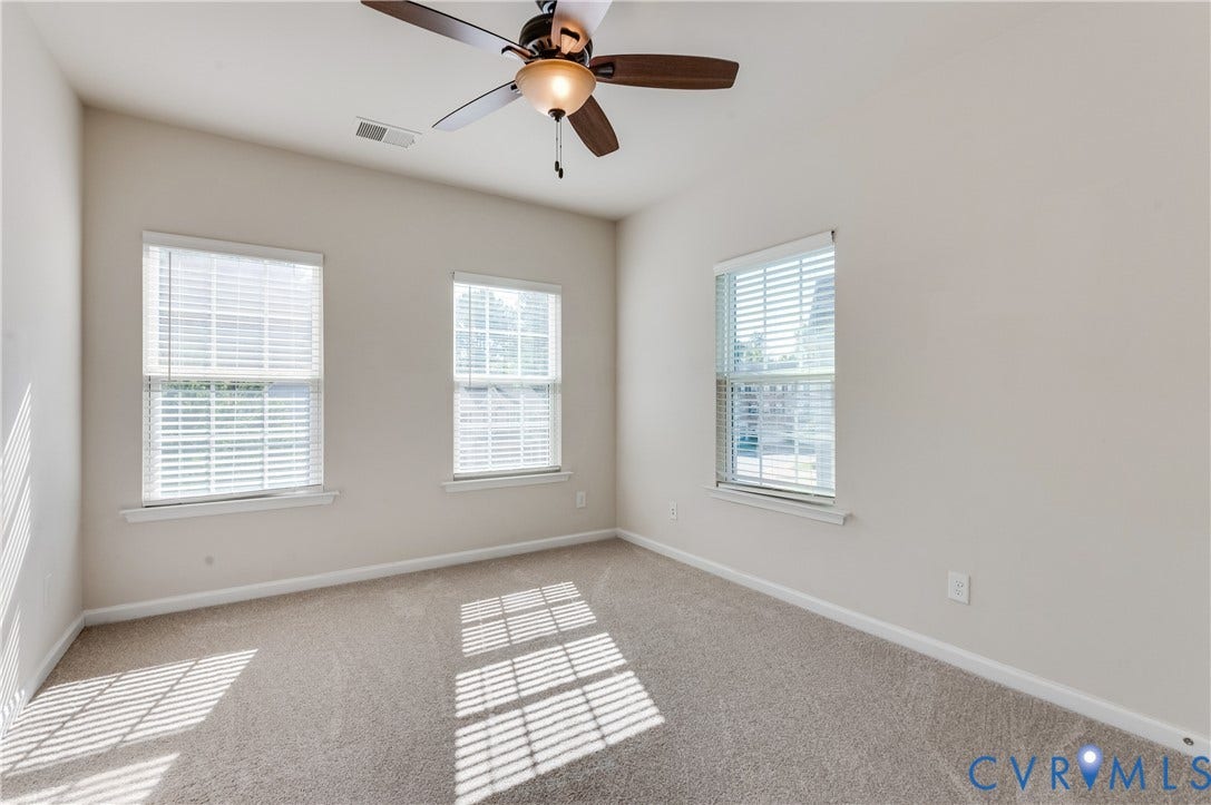 Carpeted flooring, vaulted ceiling, three windows with blinds, and a ceiling fan with light fixture