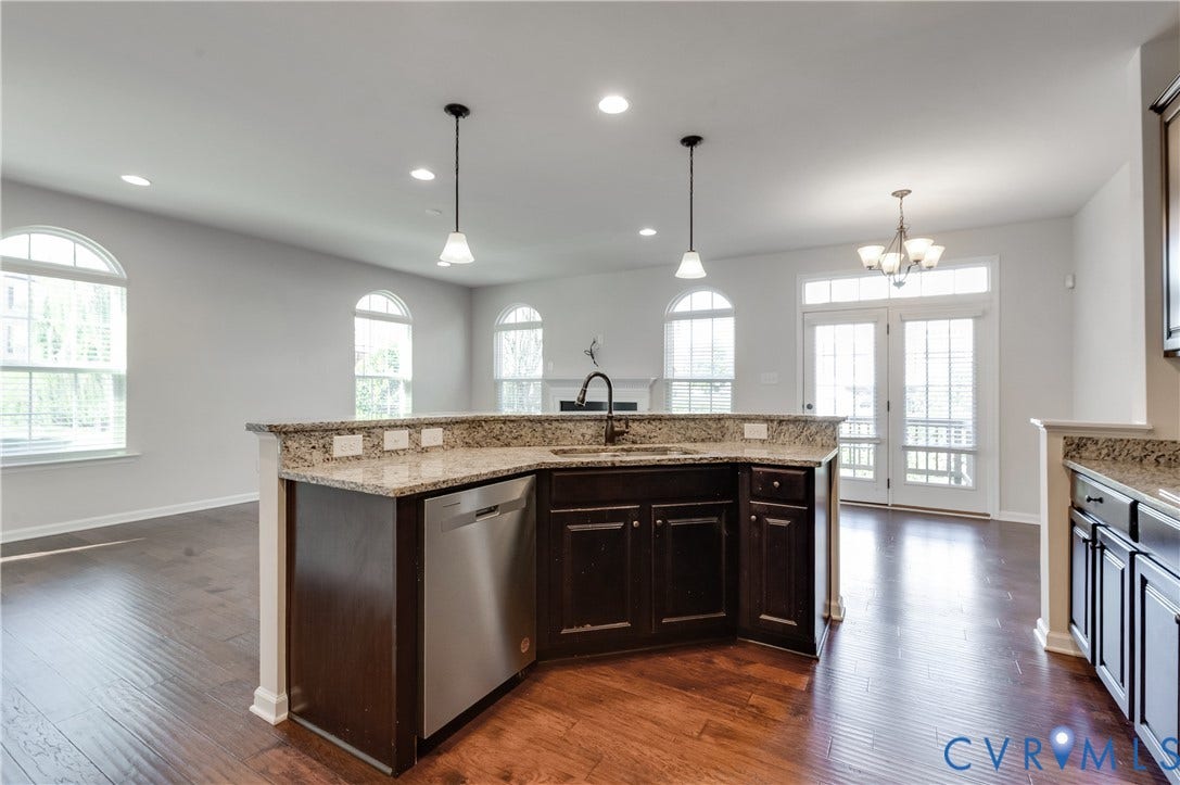 Kitchen island featuring granite countertops, a built-in sink, and a stainless steel dishwasher