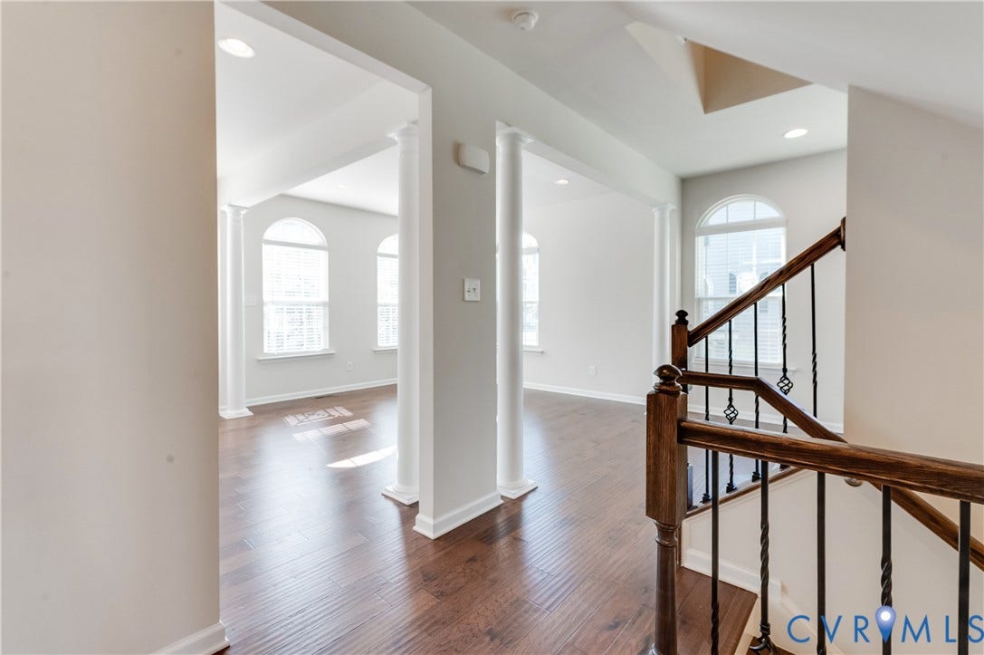 Hardwood flooring, arched doorways, decorative columns, arched windows, and a staircase with an ornamental iron railing
