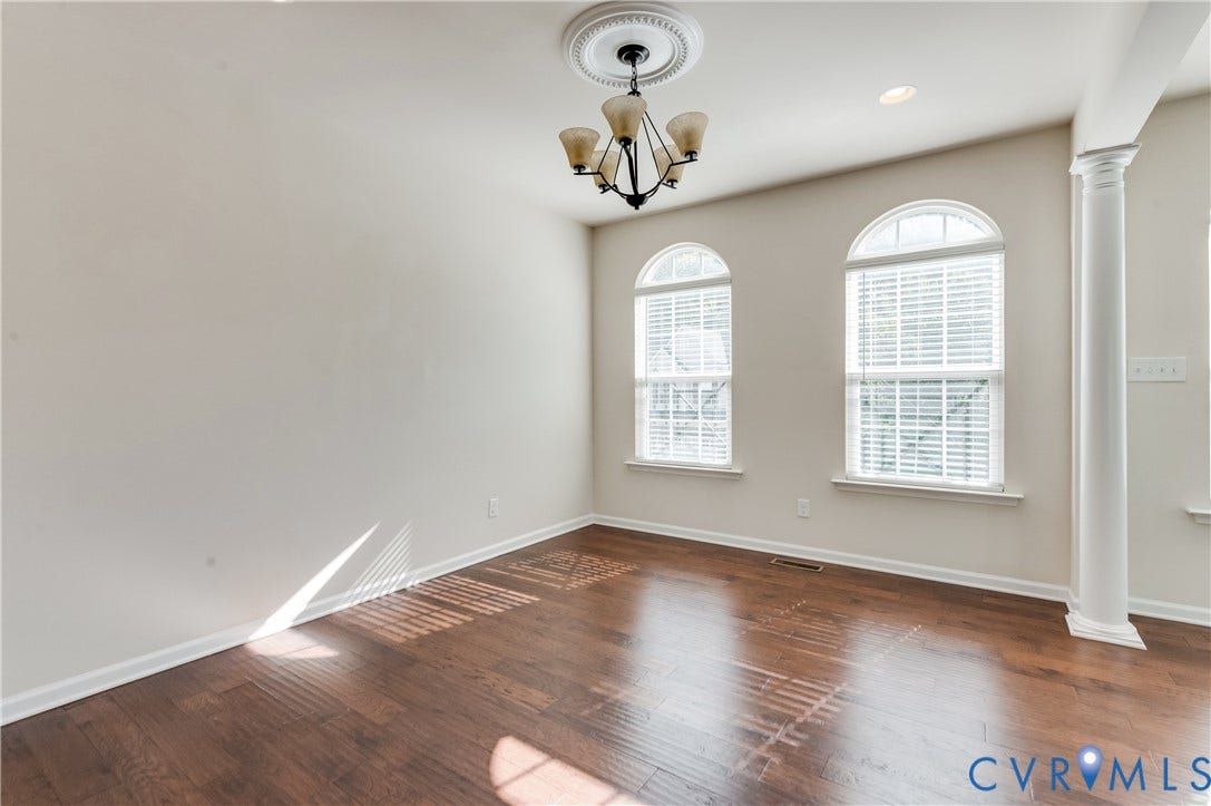Wood-finish flooring, two arched windows, recessed lighting, and a decorative column