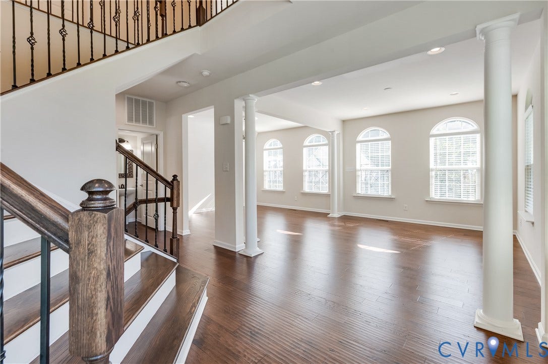 Hardwood flooring throughout, a staircase with decorative iron balusters, and multiple arched windows