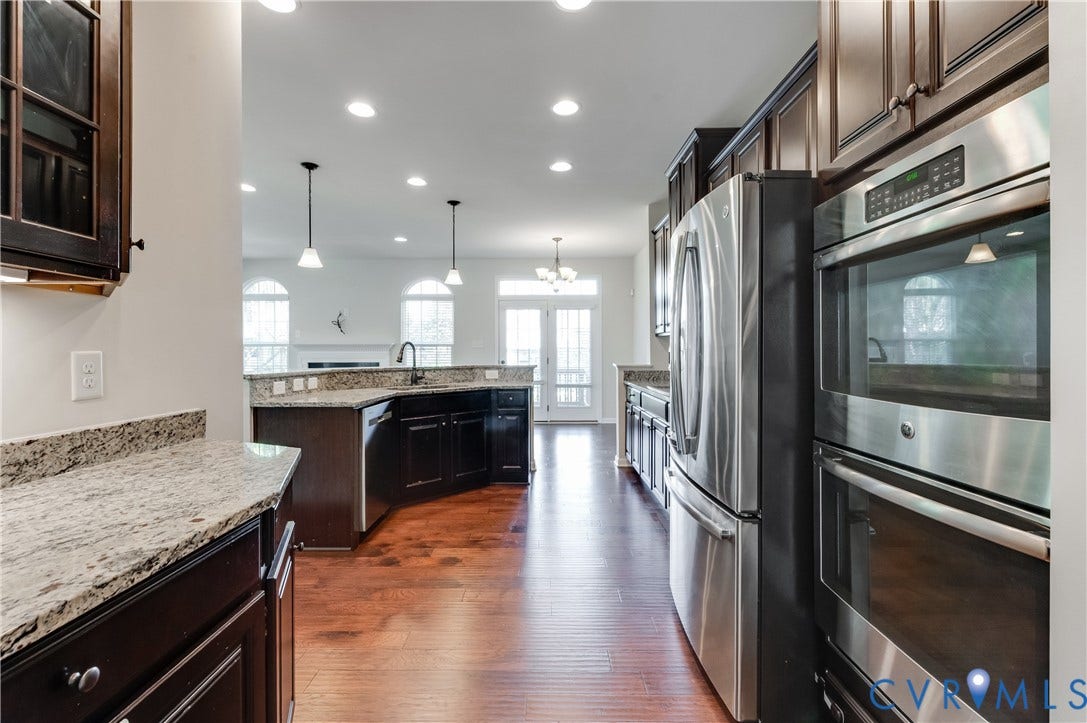 Wood-finish flooring with dark wood cabinetry, granite countertops, and stainless steel appliances