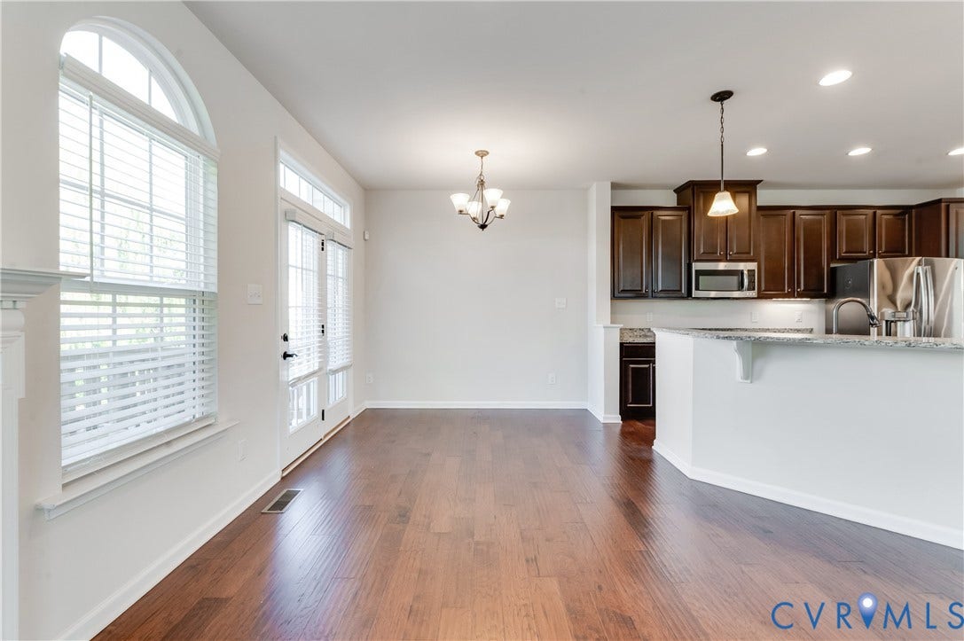 Wood-finish flooring throughout, arched window with blinds, double glass-paneled door, recessed lighting, and a kitchen featuring dark wood cabinetry and a peninsula countertop