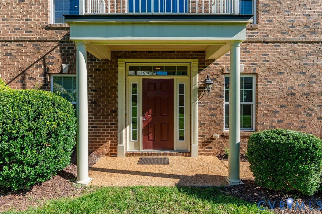 Brick exterior with covered front entry, flanked by decorative columns, and a rich red entry door with sidelights