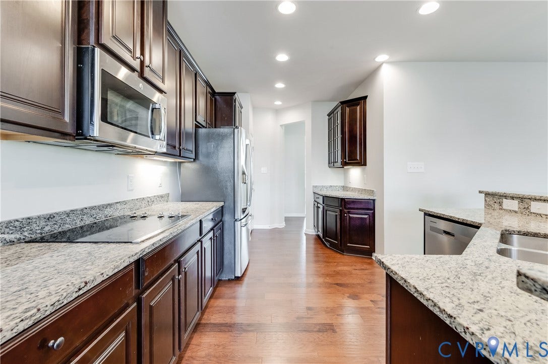 Kitchen featuring dark wood cabinetry, light granite countertops, stainless steel appliances, wood-finish flooring, and recessed lighting