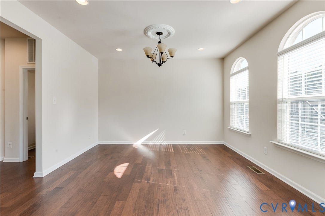 Wood-finish flooring, recessed lighting, chandelier with decorative ceiling medallion, and arched windows with blinds