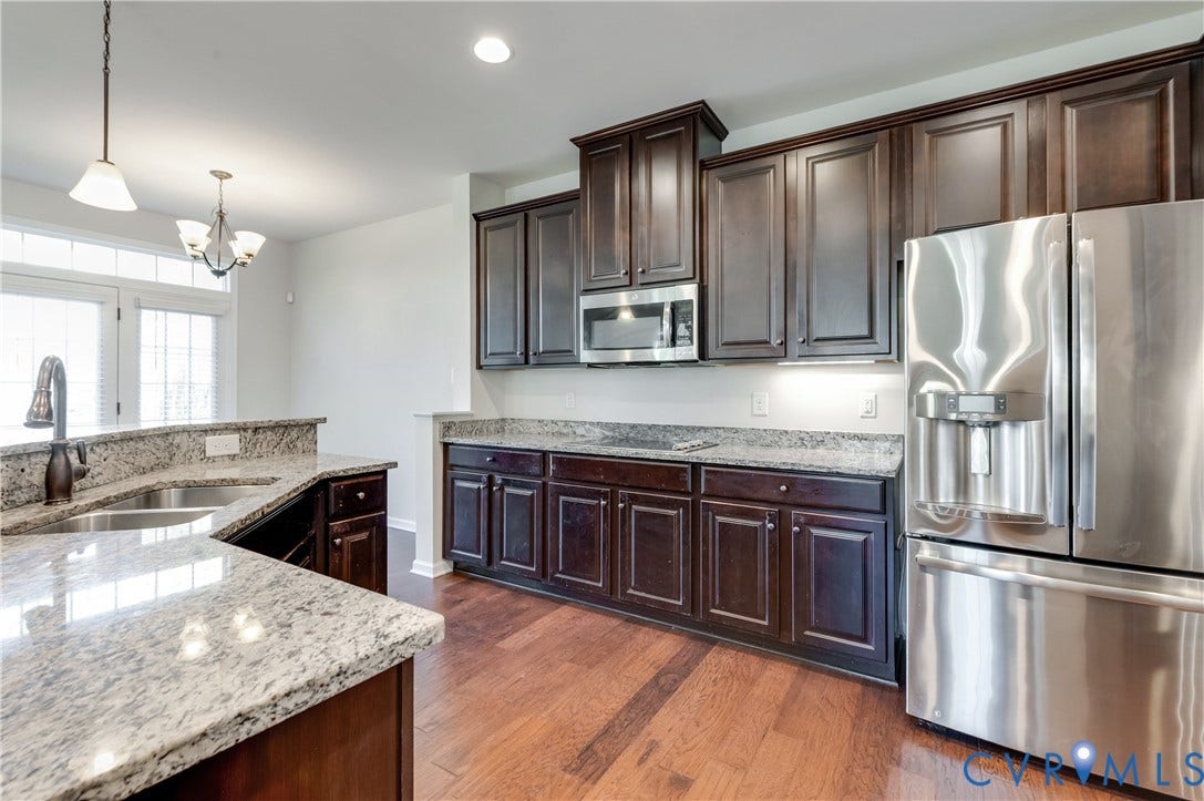Hardwood-finish flooring, dark wood cabinetry, light-toned stone countertops, stainless steel appliances, and a double basin sink