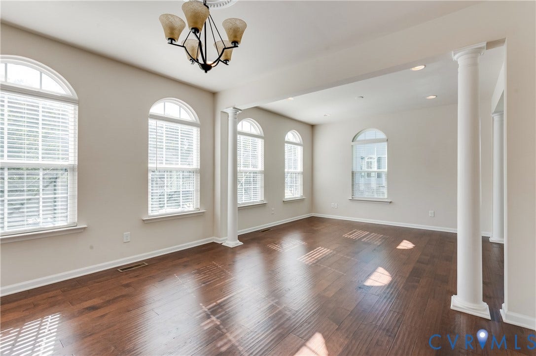 Rich wood-finish flooring, architectural columns, multiple arched windows, recessed lighting, and a decorative ceiling fixture