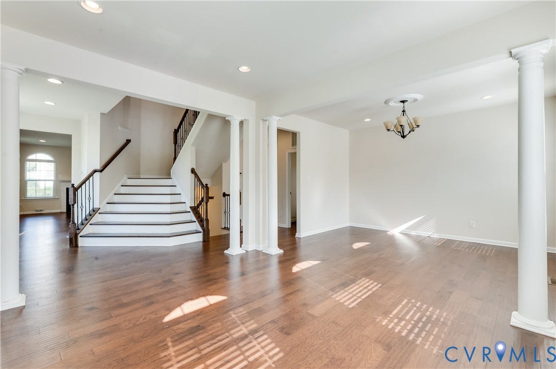 Hardwood-style flooring throughout, prominent staircase with dark wood-finish handrails and wrought iron balusters, recessed lighting, and a decorative chandelier with a ceiling medallion
