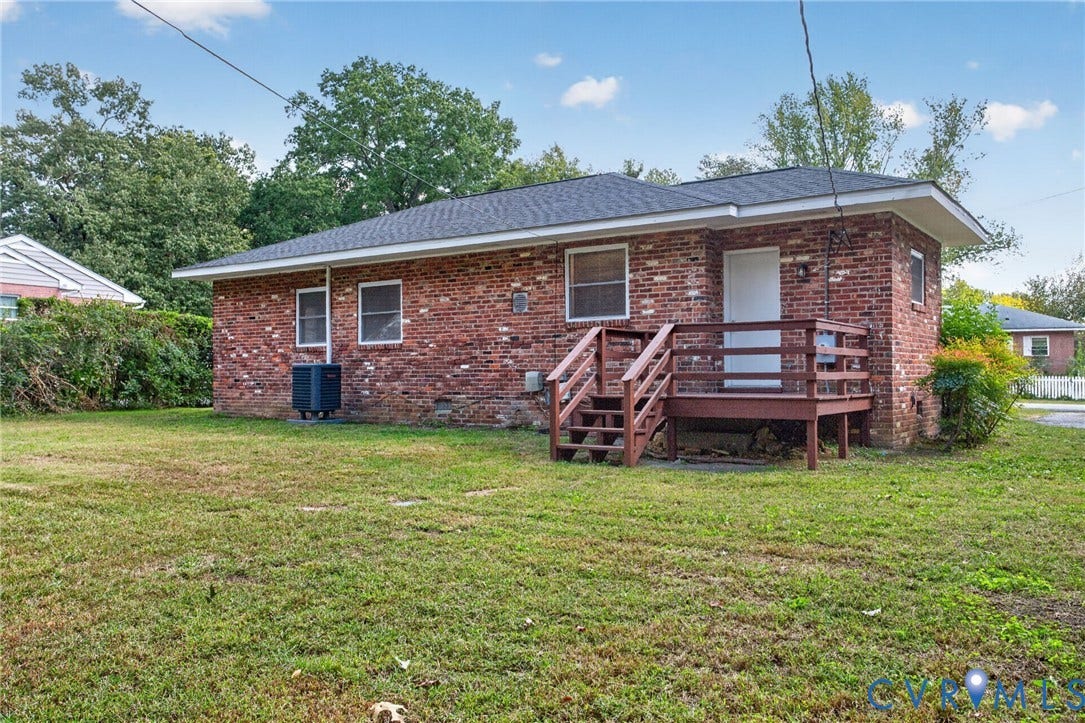 1118 Andros Road, Richmond, VA 23225 Red brick exterior featuring a black shingle roof, a rear wood deck with railing, and a ground-level air conditioning unit