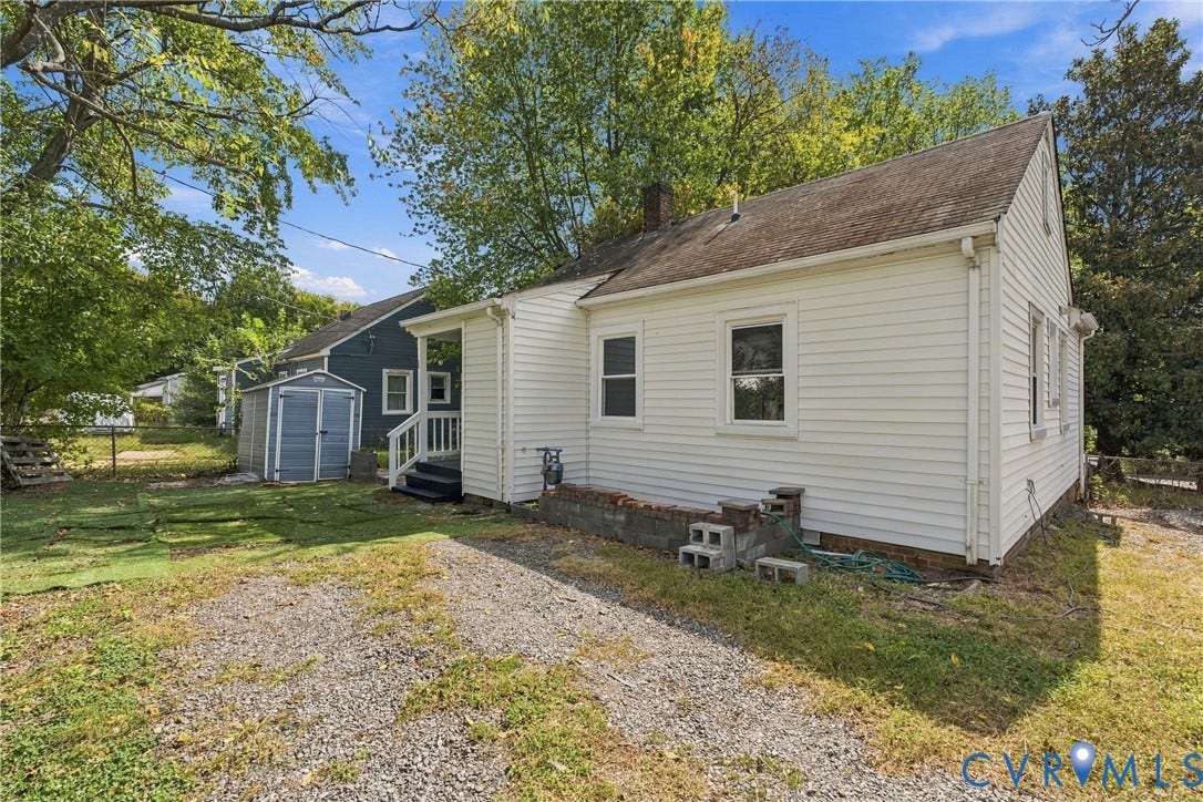 White siding exterior with a gravel driveway, rear porch, and an outbuilding
