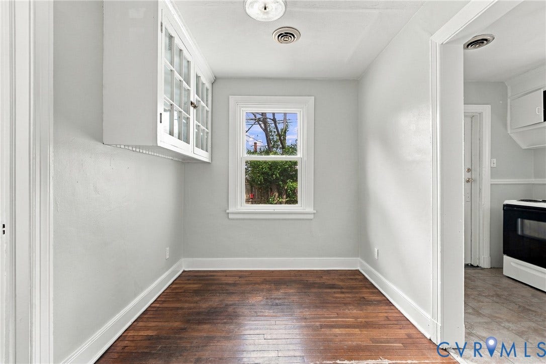 Bright hallway with warm wood-finish flooring, white painted walls, and abundant natural light from a large window