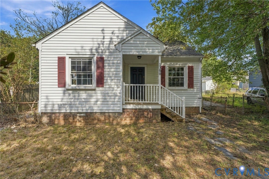 Exterior featuring horizontal white siding, red window shutters, a covered front porch with white railings, and a dark front door