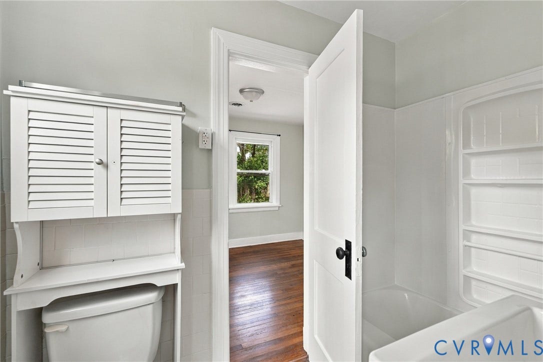 White louvered cabinet, white tiled bathtub surround, and a white interior door with black hardware