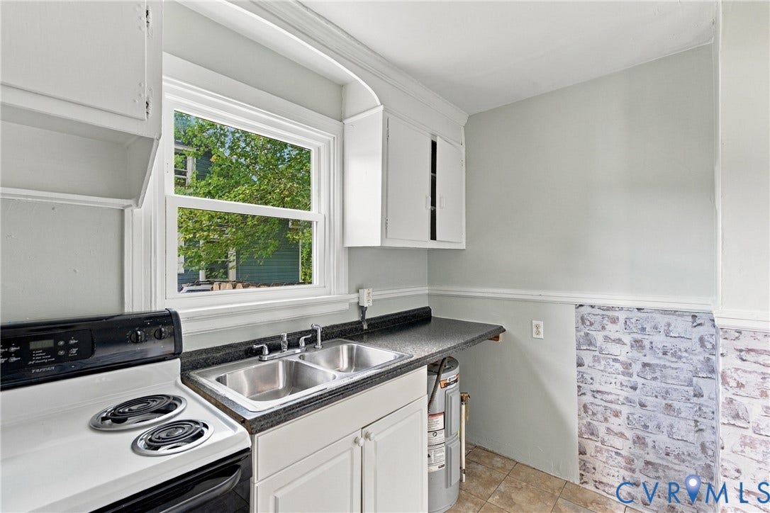 Double basin stainless steel sink with black countertop, white cabinetry, and a white electric range