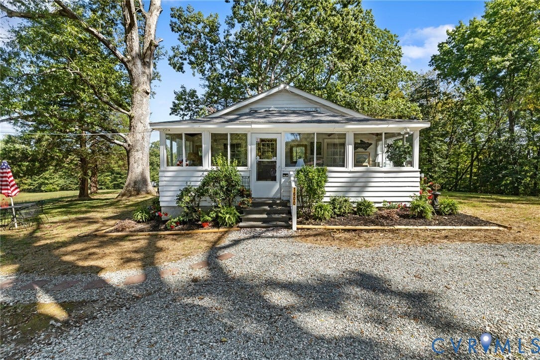 White siding exterior with a screened porch, gravel driveway, and mature landscaping.