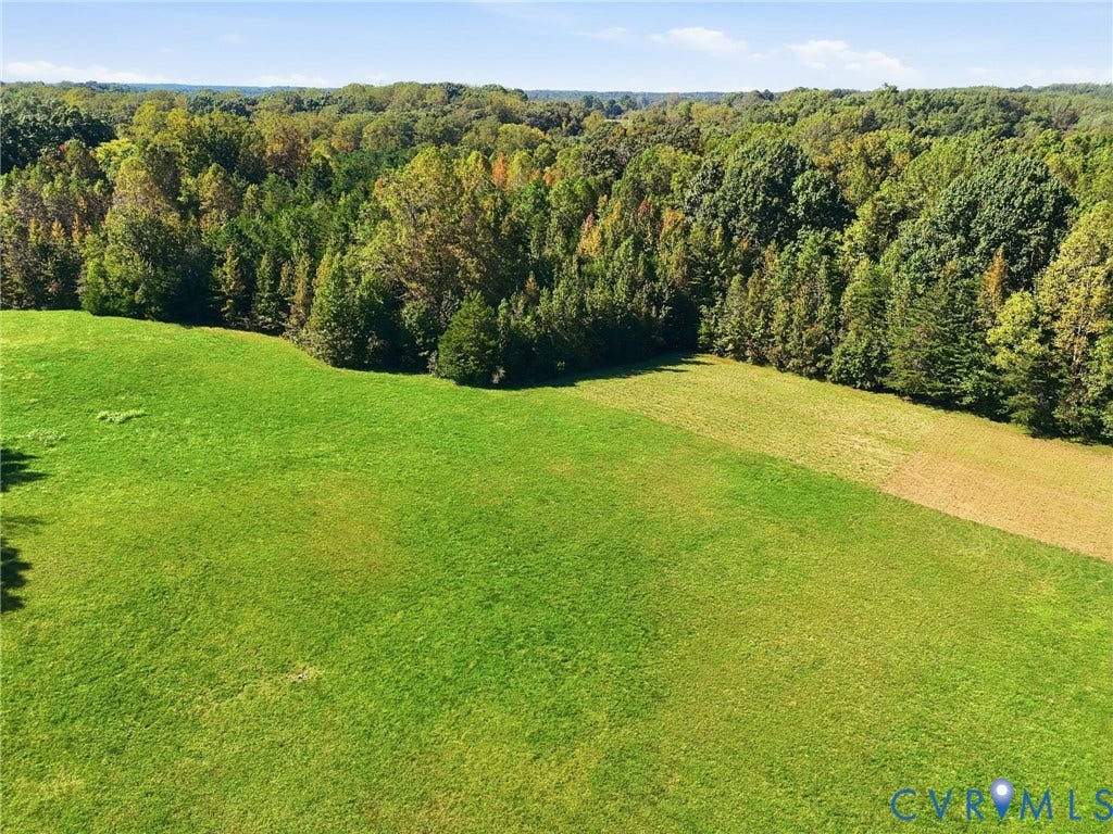 Expansive green field bordered by mature trees.