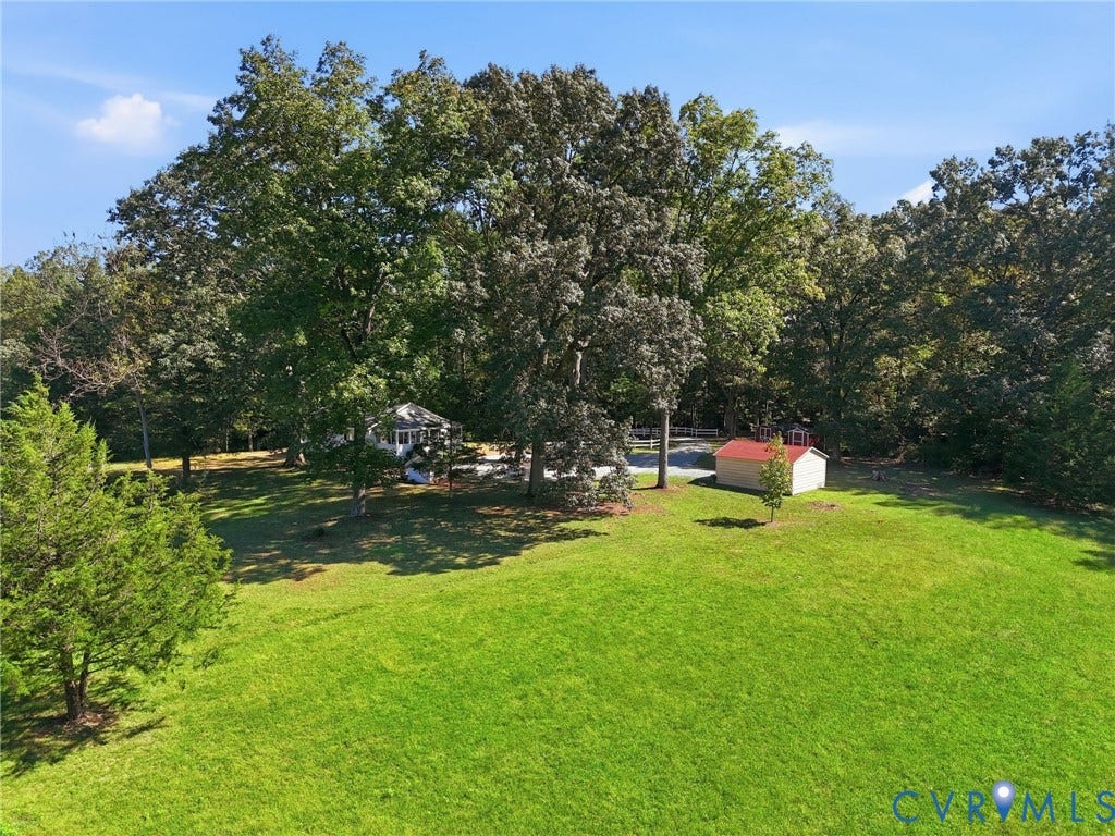 Expansive green lawn, mature trees, white privacy fence, red-roofed shed, and a gazebo structure.