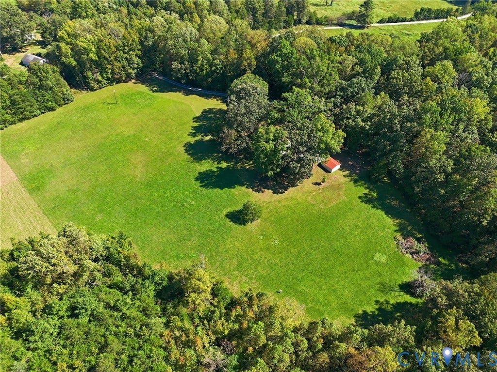 Expansive green acreage featuring a compact red-roofed outbuilding and abundant mature trees.