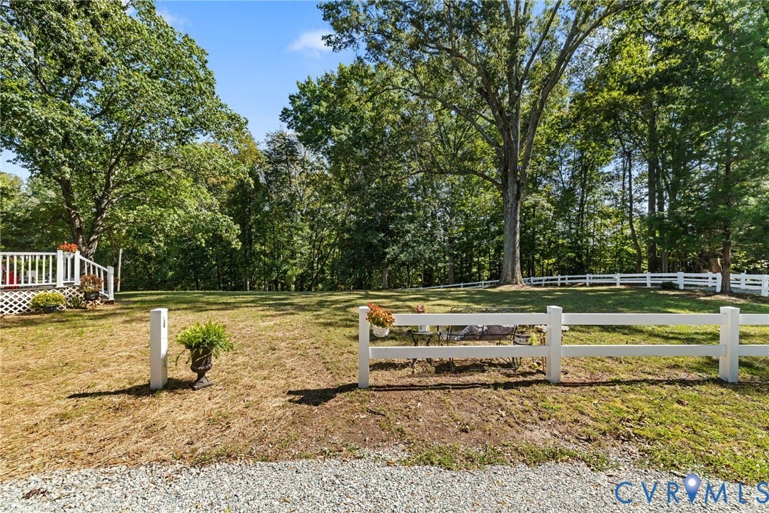 Expansive yard with mature trees, white picket fencing, and a gravel driveway.