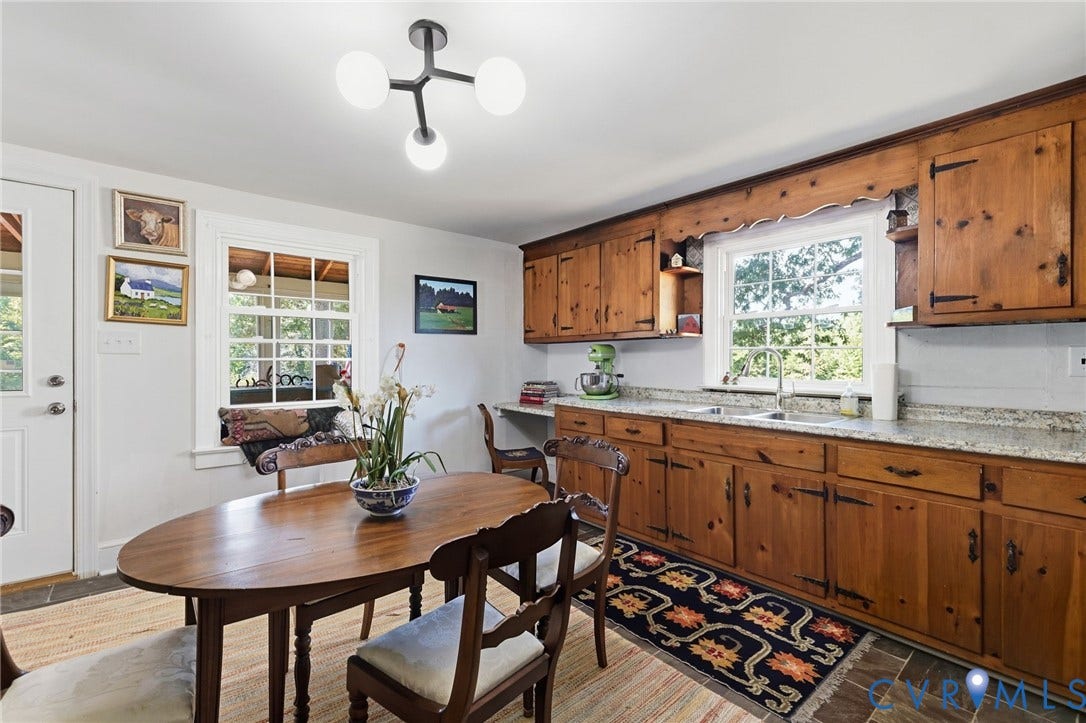 Wood cabinetry with black hardware, stone countertops, a stainless steel sink with a gooseneck faucet, window-mounted lighting, and slate-finish flooring.