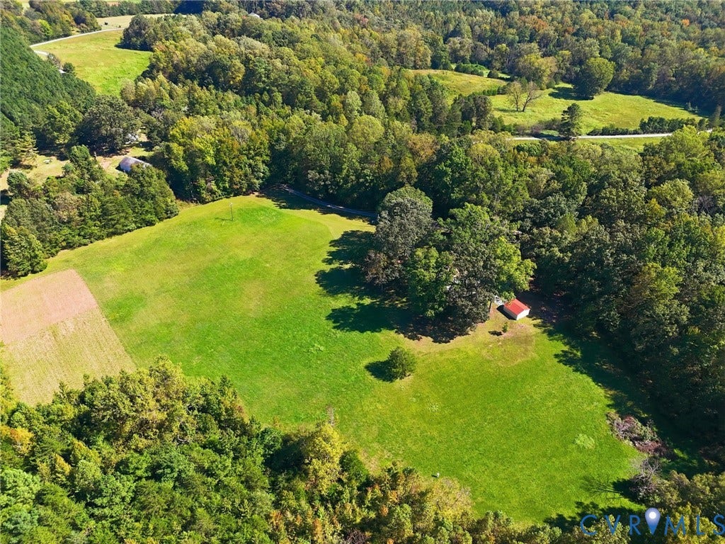 Expansive green spaces surrounded by mature trees, featuring a red-roofed outbuilding and cultivated land.