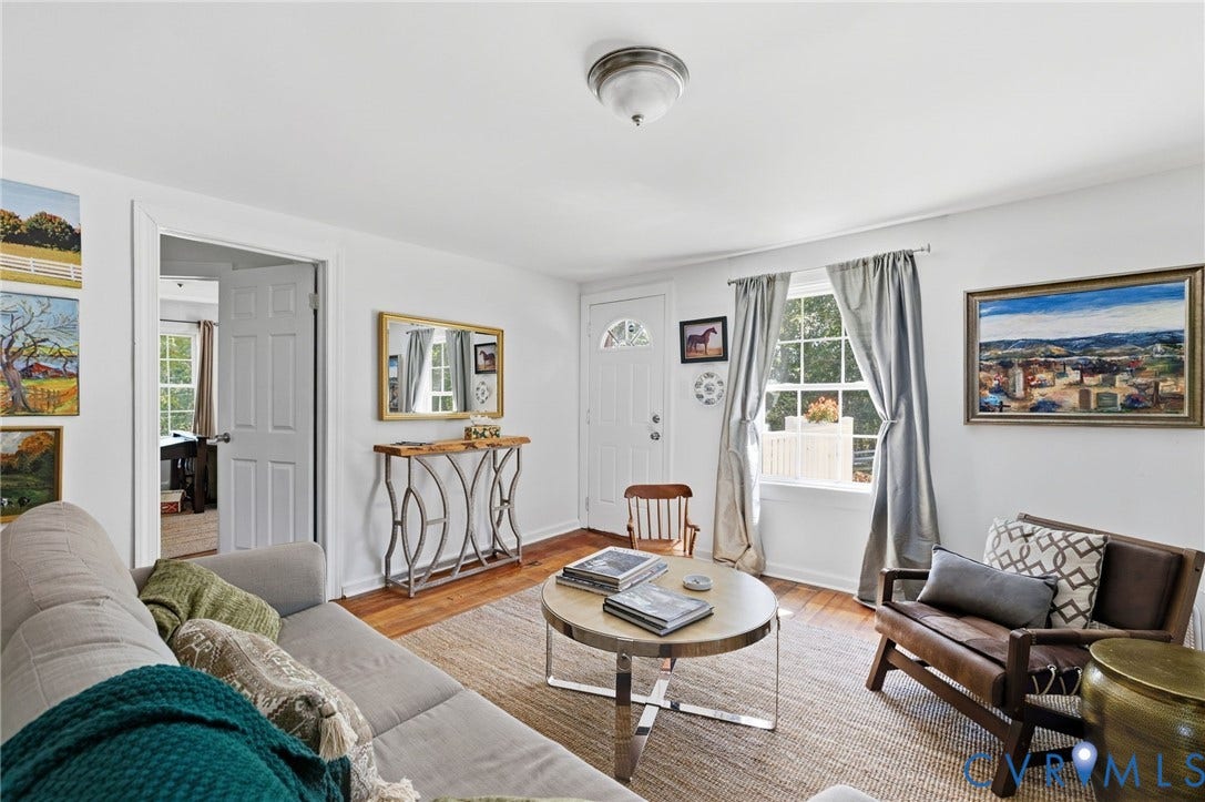 Hardwood flooring, white painted walls, natural light through a double window, and a white paneled door.