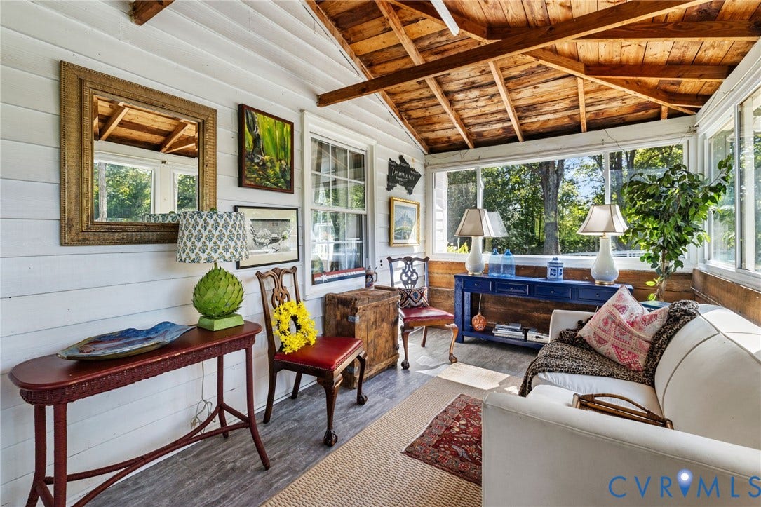 Exposed wood beam ceiling, white plank walls, large pane windows, wood-finish flooring, and a blue console table.