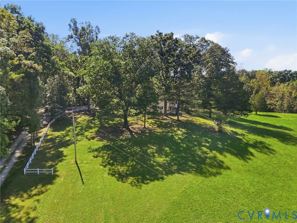 Expansive green lawn with mature trees and a white split-rail fence.
