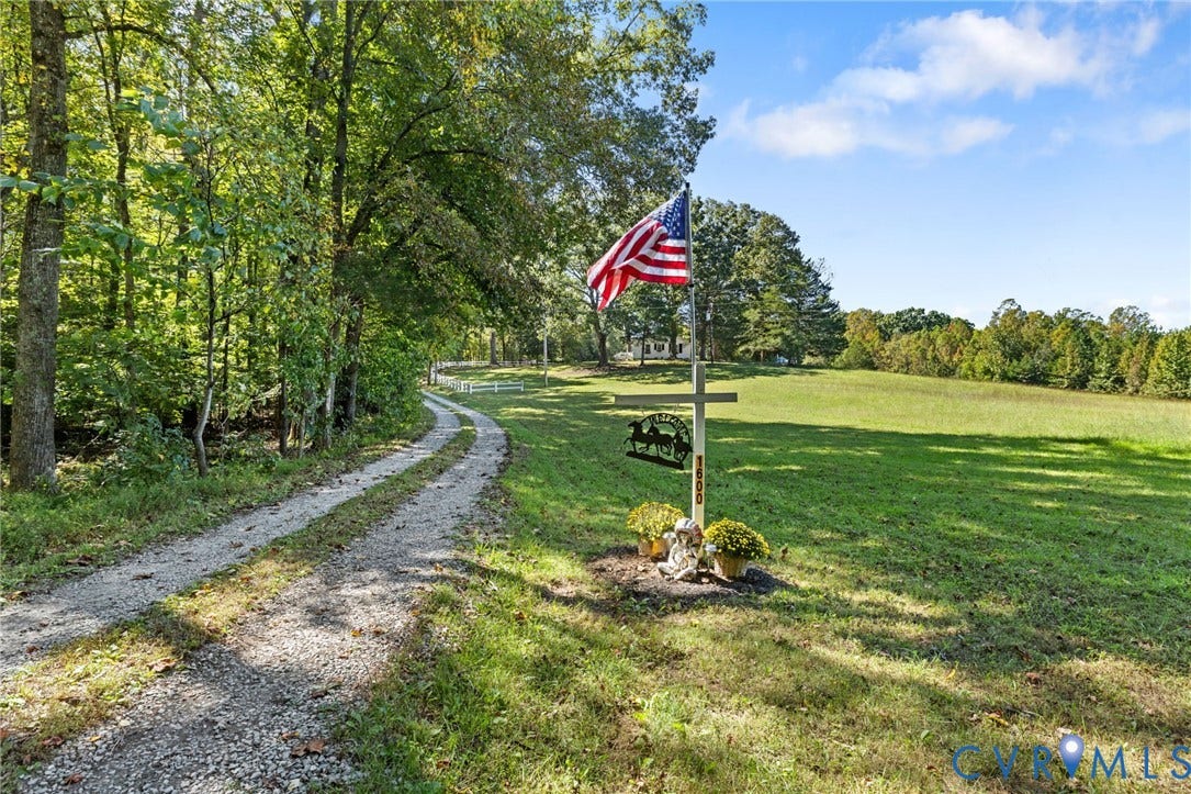 Gravel driveway bordered by mature trees and expansive green space.
