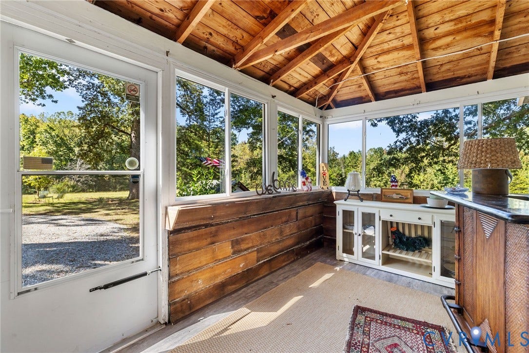 Screened porch with exposed wood ceiling beams, white trim windows, and wood-finish flooring.