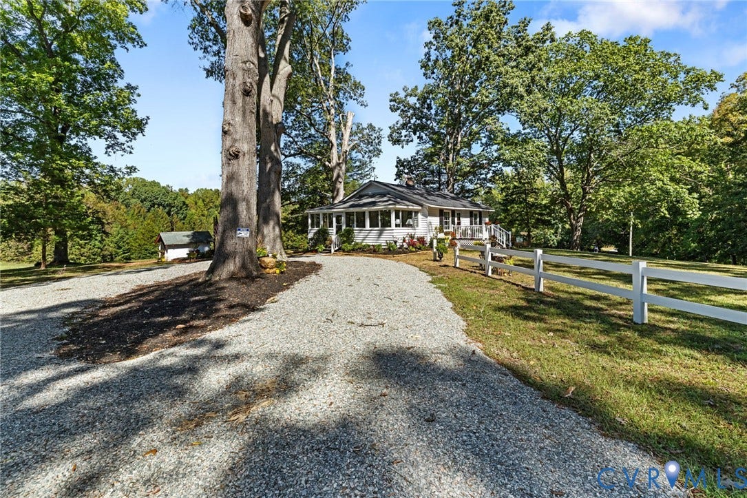 Gravel driveway leading to a residence with white siding, dark roof, and a covered porch.