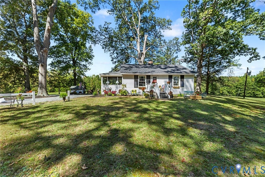 White siding with dark shutters, front entry porch, and a lush green lawn.